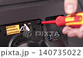 A person tightening a screw on a monitor stand bracket with a red screwdriver, demonstrating the hardware installation process for a desktop display setup in a technical workspace 140735022