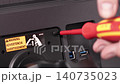 Technician using a screwdriver to tighten a screw on a computer monitor stand, illustrating technical maintenance or assembly service for modern professional electronic hardware. Zoom 140735023