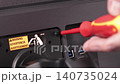 A person unscrewing the back panel of a black computer monitor using a red screwdriver for hardware maintenance, repair, or upgrade in a professional electronics workshop setting 140735024