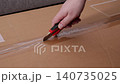 Hand using a utility knife to slice through adhesive tape on a brown cardboard box, conveying the process of opening a delivery or parcel during a home or warehouse unpacking task 140735025