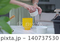 Woman sows seeds from small white bowl into yellow flower pot. Concept of home gardening 140737530