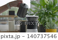 Hand pours water from kettle into paper filter set in coffee dripper on glass server 140737546