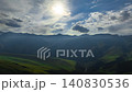 Hyperlapse from drone flying forward above mountain valley in Kyrgyzstan. Sun rays break through clouds, lighting green hills, ridges, and a narrow river below. 140830536
