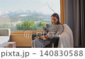 A woman reading by a large window and enjoying scenic snowy mountain view. 140830588
