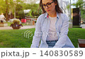 A woman sitting in the park with a laptop and working during the summer day 140830589