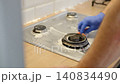 A close-up of a man wearing blue rubber gloves cleaning a foam-covered stainless steel gas stove with a sponge. Concept for professional cleaning, housework, and kitchen hygiene. copy space. Banner 140834490