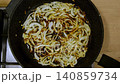 Thinly sliced onions are fried in hot oil. Cooking chopped vegetables in a frying pan. Chopped onions are fried on the stove. Close-up: frying, browning, seasoning. Food preparation. Cooking. 140859734