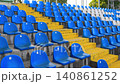 Spectator seats in the stands for football fans with blue and white chairs at the football stadium at sunset. Hand-held video. 140861252