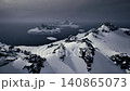 snowy mountain ridge overlooking icy sea, dark clouds and scattered ice floes, jagged black cliffs, low light mood, remote and raw wilderness. 140865073