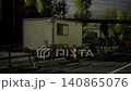 A portable trailer sits at a construction site, surrounded by barriers and safety equipment. Evening light casts a warm glow on the scene, highlighting the busy urban landscape. 140865076