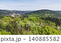 Aerial panorama of valley town framed by rolling green hills and mixed forest, winding roads and scattered 140885582