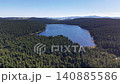 Aerial lake panorama over dense pine forest, calm blue water with curved peninsula, distant hills under clear 140885586