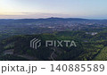 Dawn over town and forest ridges, aerial drone pans across rolling hills toward distant urban skyline, soft 140885589