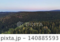 Sunset aerial over rolling conifer hills with pastel sky, warm glow on treetops, long shadows, serene evening 140885593