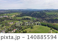 Aerial view rolling green fields village offering serene panorama with scattered cottages, winding roads, 140885594