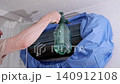Male technician cleaning and washing an indoor air conditioner unit with a water sprayer at home 140912108