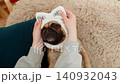Hand wiping pug dog face with soft wet tissue on sofa, gentle cleaning care with calm relaxed pet 140932043