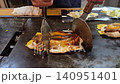 Cooking and cutting Okonoiyaki on teppan iron plate Osaka Japan traditional food 140951401