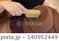 Close-up hands brush a brown felt hat indoors, focusing on dust removal, texture, and careful wardrobe maintenance. 140952449