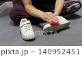 Hands scrub dirt from a white sneaker while the person sits on a gray tile floor. 140952451
