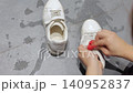 Hands wipe a white sneaker with a red sponge in a close indoor shoe care view. 140952837