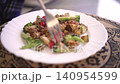 A person sits at a table and eats a plate of grilled vegetables and chicken. The food includes pieces of broccoli, tomatoes, and lettuce. It is a bright day. 140954599