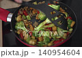 Sliced bell peppers and tofu are cooked with broccoli and onions in a frying pan. The heat creates steam as the ingredients mix together in a home kitchen setting. 140954604