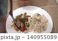 The chef prepares a dish with diced vegetables and creamy sauce. The chef serves food on a white plate while standing in the kitchen during the evening hours. 140955089