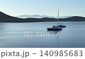 A wide, peaceful view of a calm blue bay featuring anchored luxury yachts, a rowing team in a scull boat, and scenic rolling hills beneath a clear morning sky. High quality 4k footage 140985683