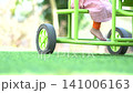 A low angle close up view of a child riding a bright green tricycle on a lush green grass lawn in a park. 141006163