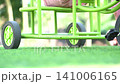 A low angle close up view of a child riding a bright green tricycle on a lush green grass lawn in a park. 141006165