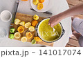 person preparing smoothie with spoon in bowl on kitchen countertop top-down perspective focused and concentrated healthy lifestyle food preparation commercial natural light clean background. 141017074