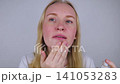 Woman applying foundation cream to cover rosacea and sunburn on her face. Sensitive skin care, redness concealment, and soothing cosmetic treatment. Woman applying foundation cream to cover rosacea and sunburn on her face. Sensitive skin care, redness concealment, and soothing cosmetic treatment. 141053283