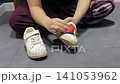 A white sneaker is cleaned with a red sponge on an indoor tiled floor with water nearby. 141053962