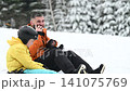 Man on a phone call with a child in a ski helmet on a snowy hill. 141075769