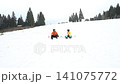 Snowboarders taking a break on a snowy mountain slope, enjoying the winter landscape. 141075772