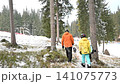 Snowboarders walking through a snowy forest after a day on the slopes. Winter wonderland scenery. 141075773