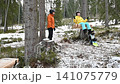 Winter fun: A child enjoys a swing in a snowy forest while an adult watches nearby, a snowboard rests against a tree. 141075779