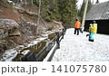 Snowboarders walking by a winter stream, near a cabin in the woods. 141075780