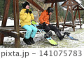 Snowboarders take a break, adjusting gear at a snowy mountainside rest stop. 141075783