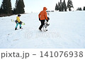 Snowboarders walking up a snowy slope towards a winter landscape. 141076938