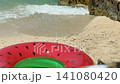 Colorful watermelon-shaped inflatable ring  on a sunny sandy beach near waves of crystal-clear turquoise water 141080420