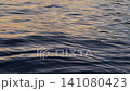 Dark ocean surface shimmering with warm golden reflections of the setting sun, waves and glowing evening light 141080423