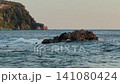Sea waves crashing against coastal rocks at sunset, with towering cliffs in the background 141080424