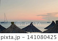 Straw beach umbrellas at sunset with sailboats on calm sea 141080425