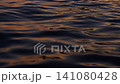 Dark ocean surface shimmering with warm golden reflections of the setting sun, waves and glowing evening light 141080428