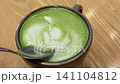 Scooping fluffy foam from matcha latte with teaspoon in gray ceramic cup 141104812