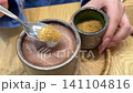 Adding brown cane sugar to hot cocoa in ceramic cup on cozy kitchen table 141104816