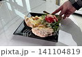 Two slices of cheese pizza and fresh arugula salad with cherry tomatoes and almond flakes on black square plate, golden fork on white table, tasty lunch and snack concept 141104819