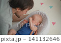 Father talking to sleepy baby son in baby nest on floor. 141132646
